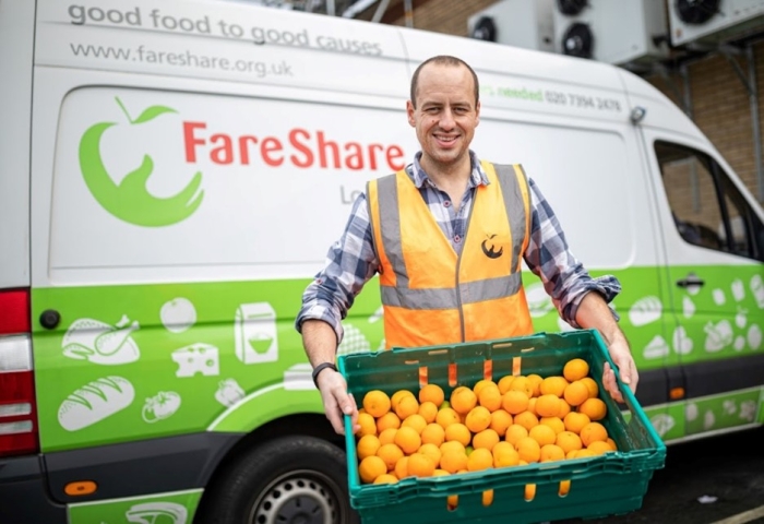 Image of a FareShare worker holding a crate of oranges in front of a FareShare van